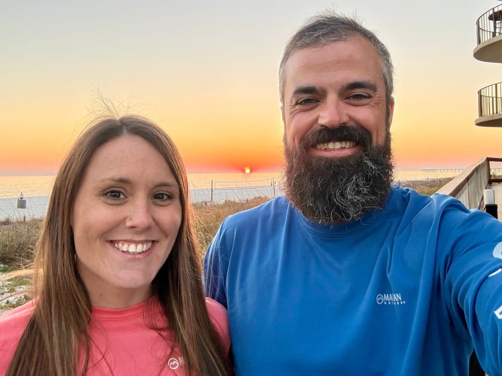 The hosts smiling on the beach at sunset