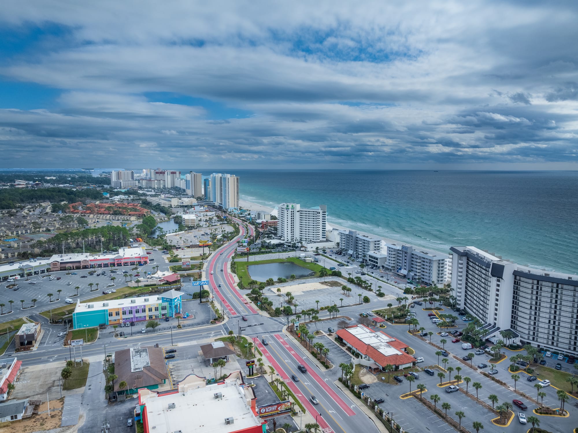 Aerial of the Panama City Beach coastline, with the gulf, beachfront towers, and the road inland.