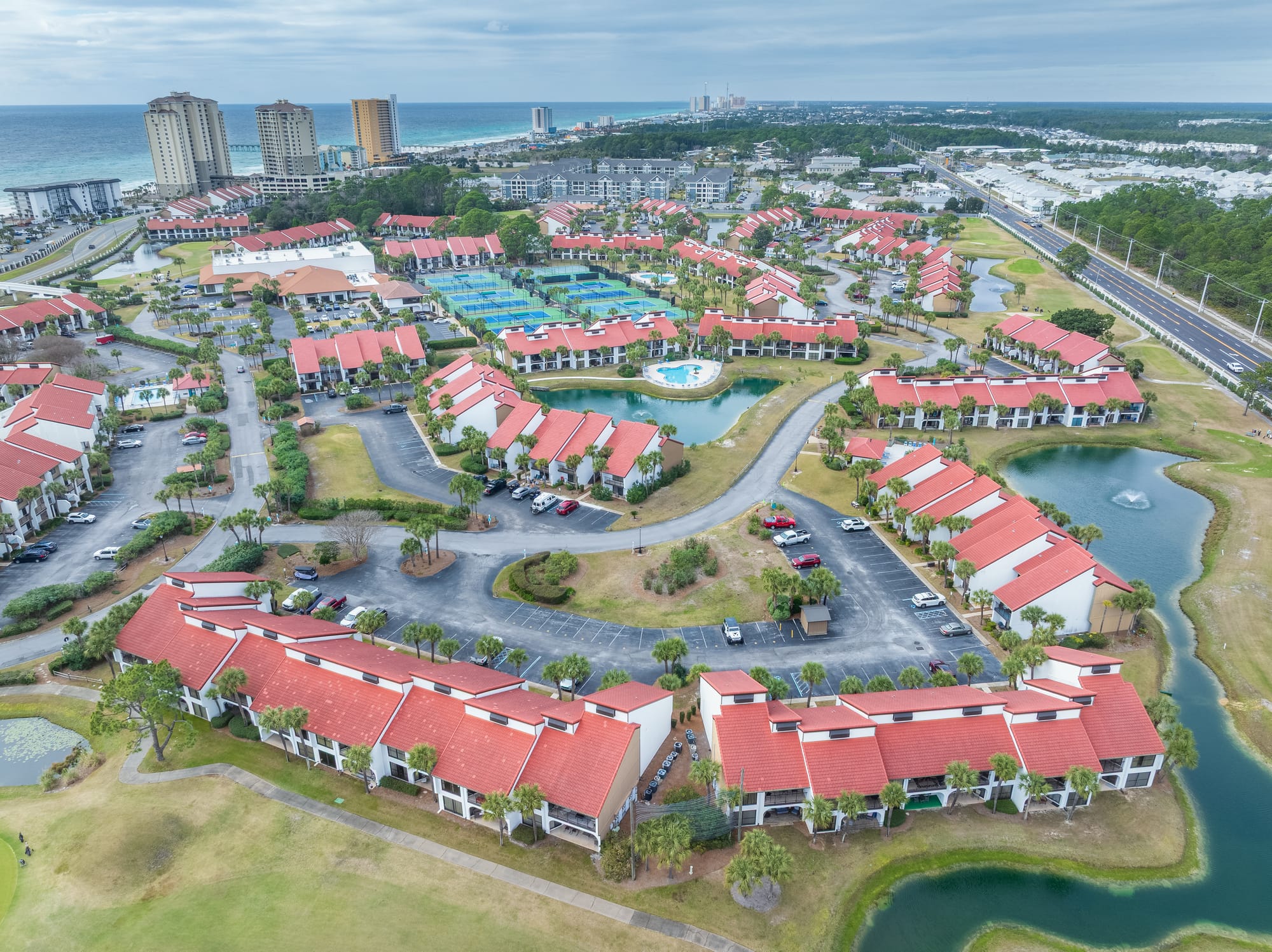 Aerial of red-roof Golf Villas, ponds, tennis courts, and the gulf in the distance.