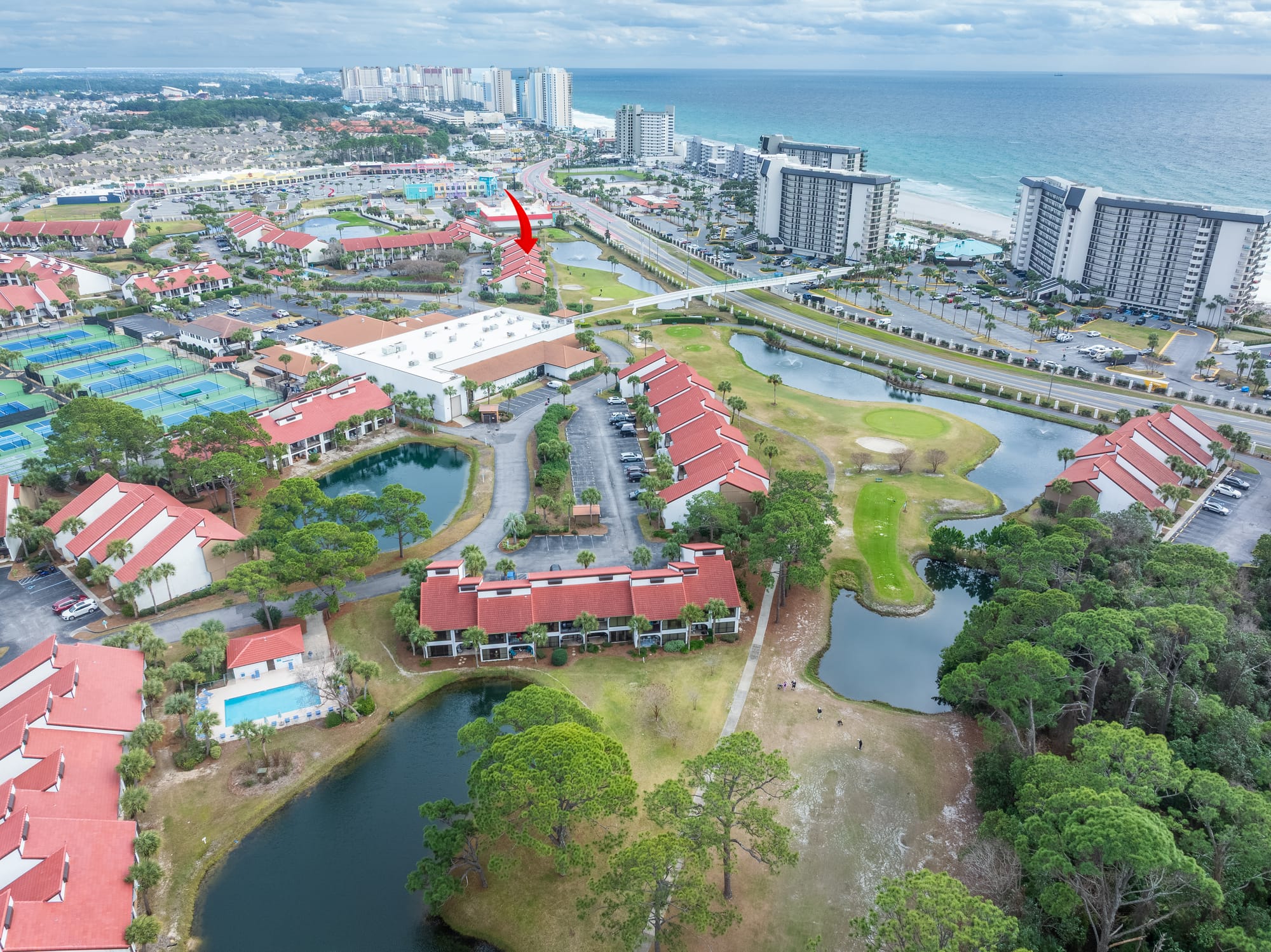 Aerial of the community, ponds, and gulf. A red arrow points toward buildings near the road.
