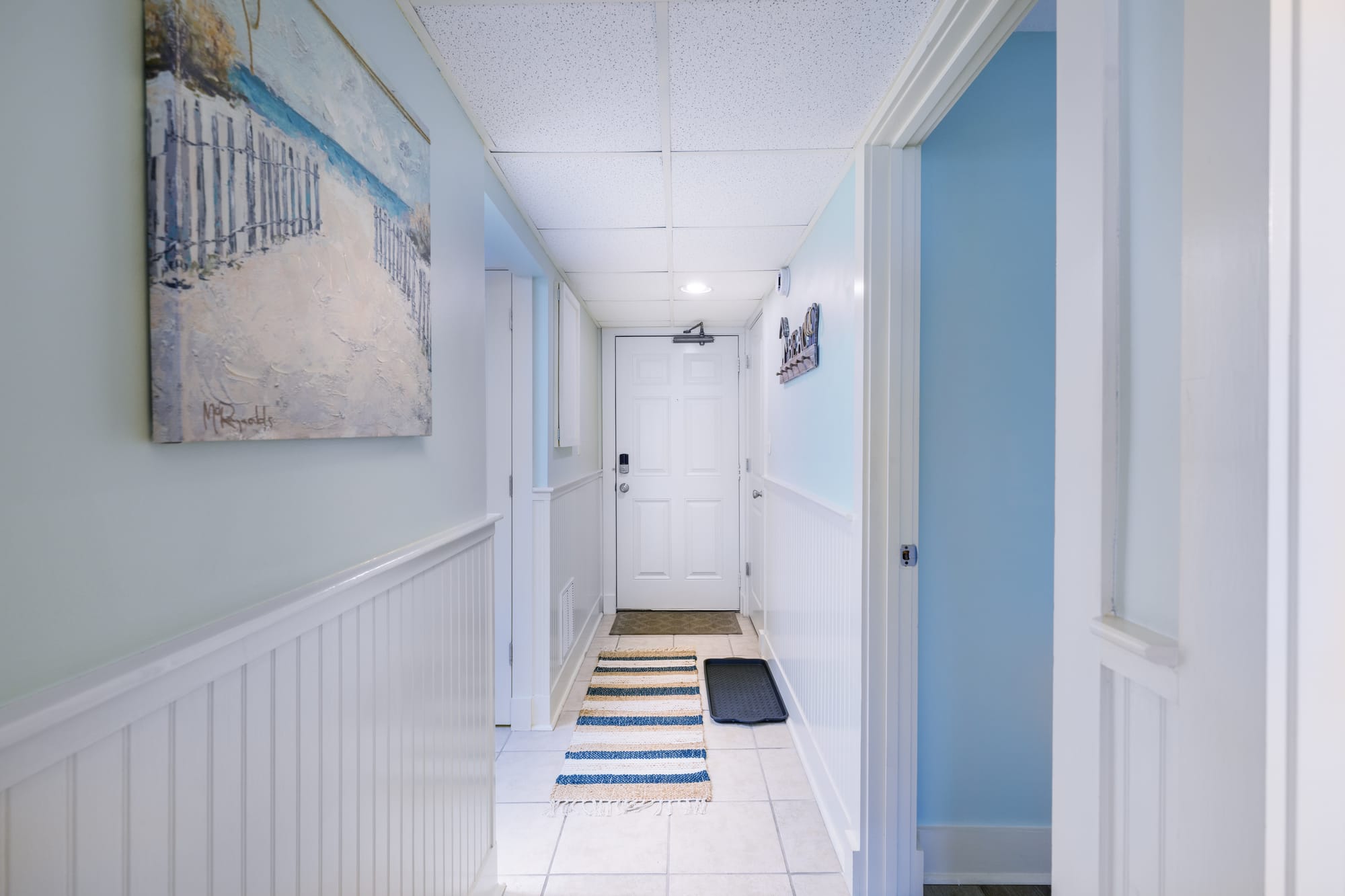Hallway looking toward the front door, with tile floors and white wainscoting.