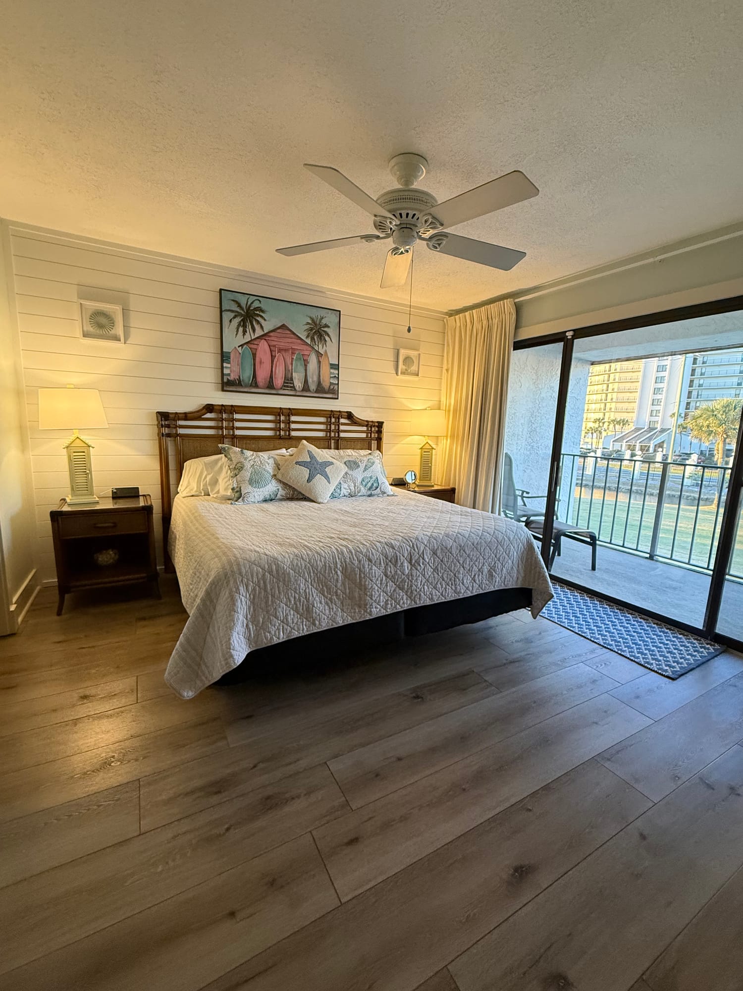 Master bedroom with a king bed, white quilt, shiplap wall, and a sliding door to the balcony.