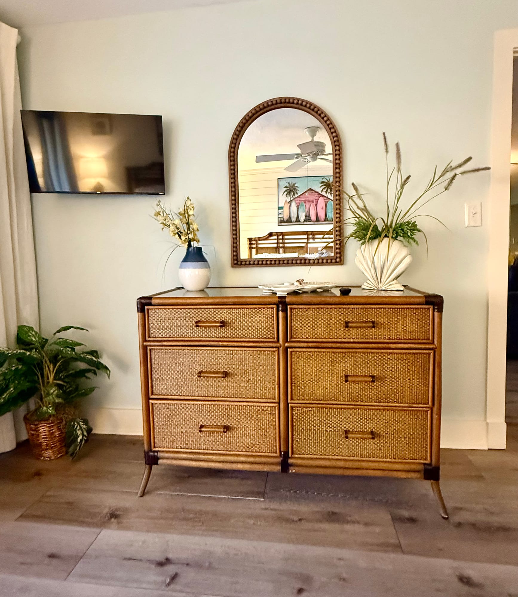 Rattan dresser, arched mirror, and wall-mounted television in the master bedroom.