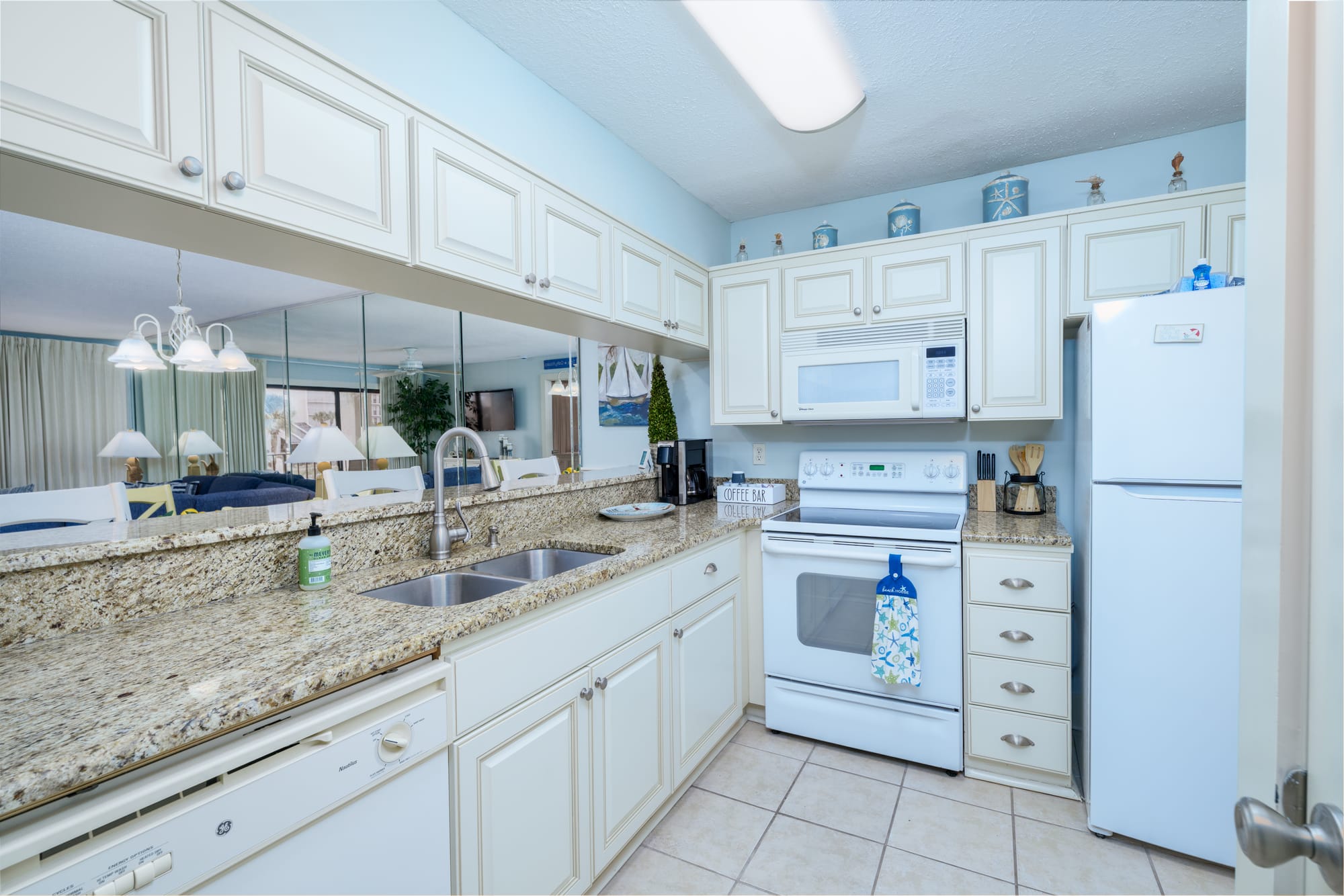 Galley kitchen with white cabinets, a double sink, electric range, microwave, and refrigerator.