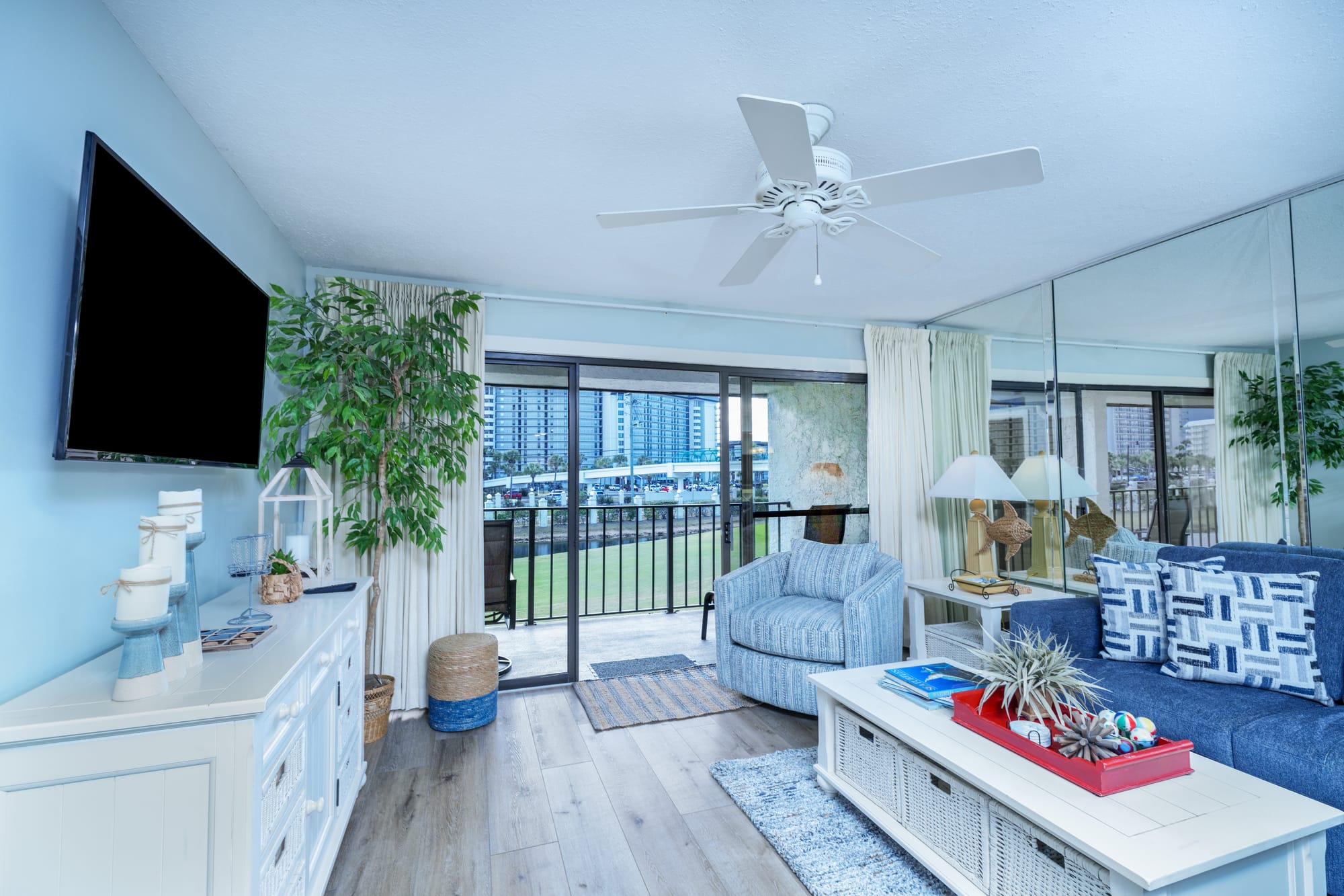 Living room with a wall-mounted television, white dresser, armchair, and open balcony doors.