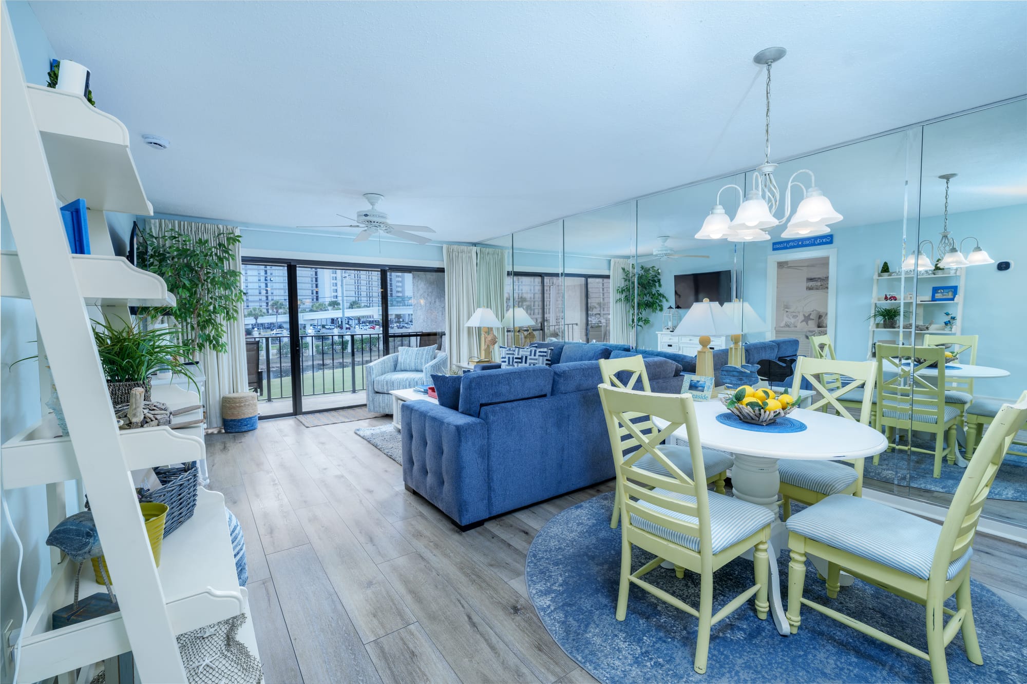 Dining table in the foreground and the living room sofa and balcony doors beyond it.