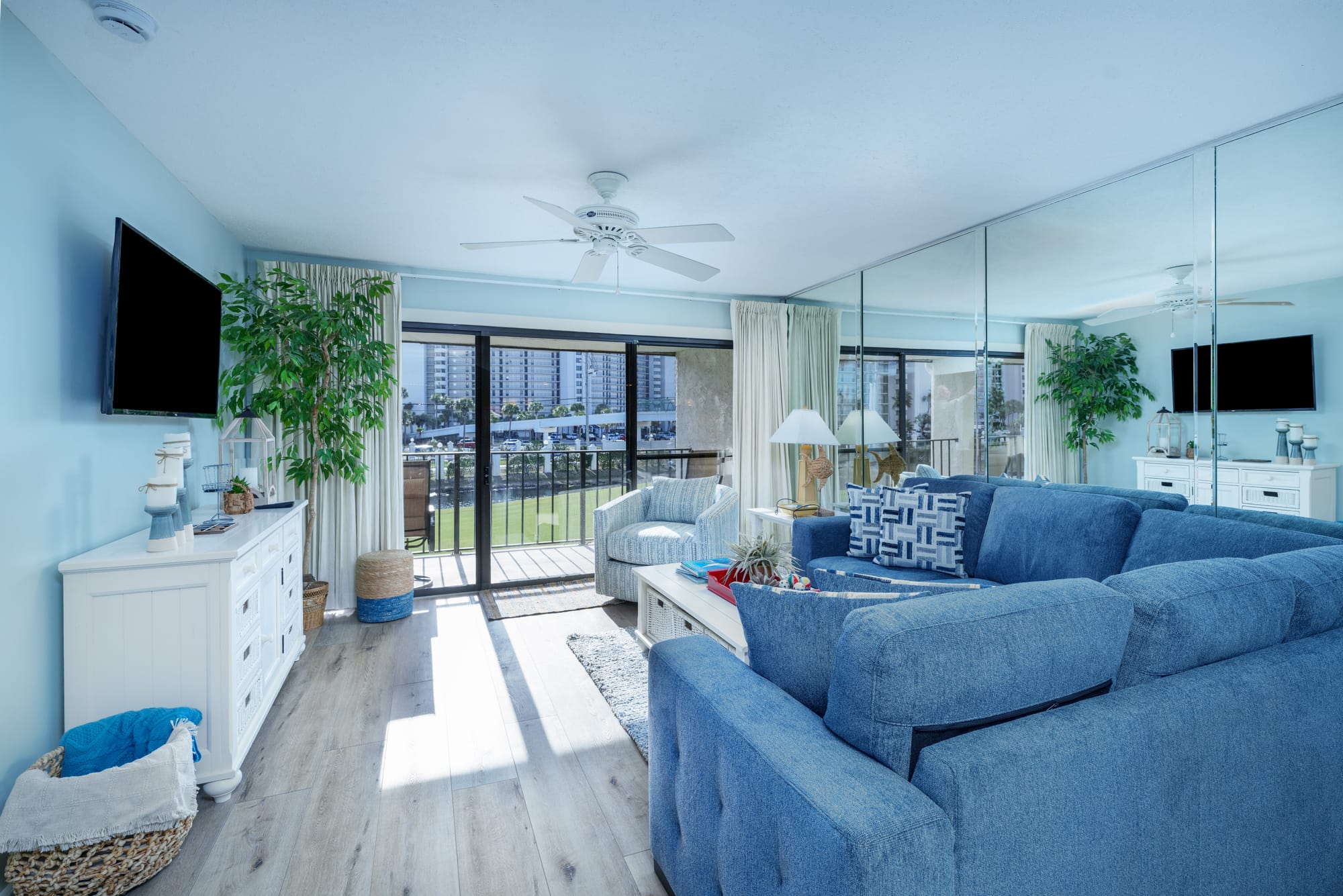 Living room with a blue sectional, white coffee table, television, and sliding glass doors to a balcony.